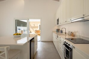 A modern kitchen with white cabinetry, a black countertop, and a view into the dining area.