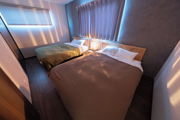 Ein Hotelzimmer mit zwei Betten, einem Holz-Kopfteil, einem Nachttisch mit Lampe und einem Fenster mit Vorhängen.