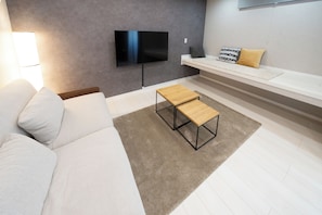 Uma sala de estar moderna com sofá, mesa de centro, TV de tela plana na parede e um banco com almofadas.