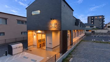 Un edificio moderno con un letrero que dice 'NOMAD BASE MEINOHAMA' y un área de estar al aire libre techada.