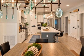 A modern kitchen with a central island, pendant lights, and a dining area with a wooden table. - Beach, Pizza Oven, Saltwater Heated pool, Hot Tub (Hilton Head Island)