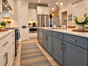 A modern kitchen with white and blue cabinetry, stainless steel appliances, and a blue and brown rug. - Beach, Pizza Oven, Saltwater Heated pool, Hot Tub (Hilton Head Island)