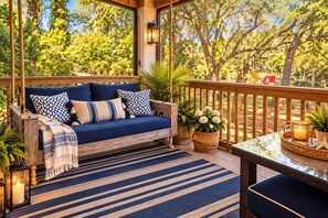 Eine Holzterrasse mit einem blauen Sofa, einem Streifen Teppich und Topfpflanzen.