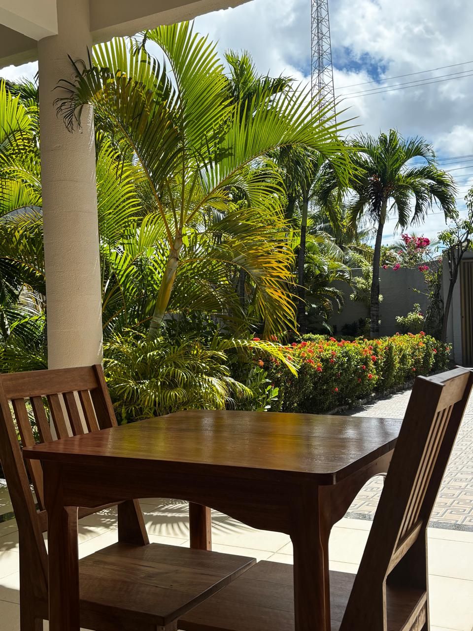An outdoor dining area with a wooden table and chairs, surrounded by lush greenery and flowering plants.