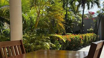 An outdoor dining area with a wooden table and chairs, surrounded by lush greenery and flowering plants.