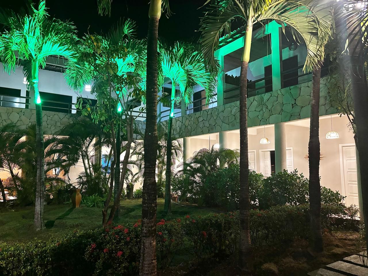 A hotel courtyard with palm trees, a stone wall, and a building with large windows.