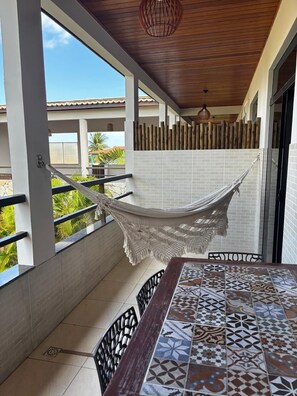 A balcony with a hammock, a tiled table, and a view of palm trees.