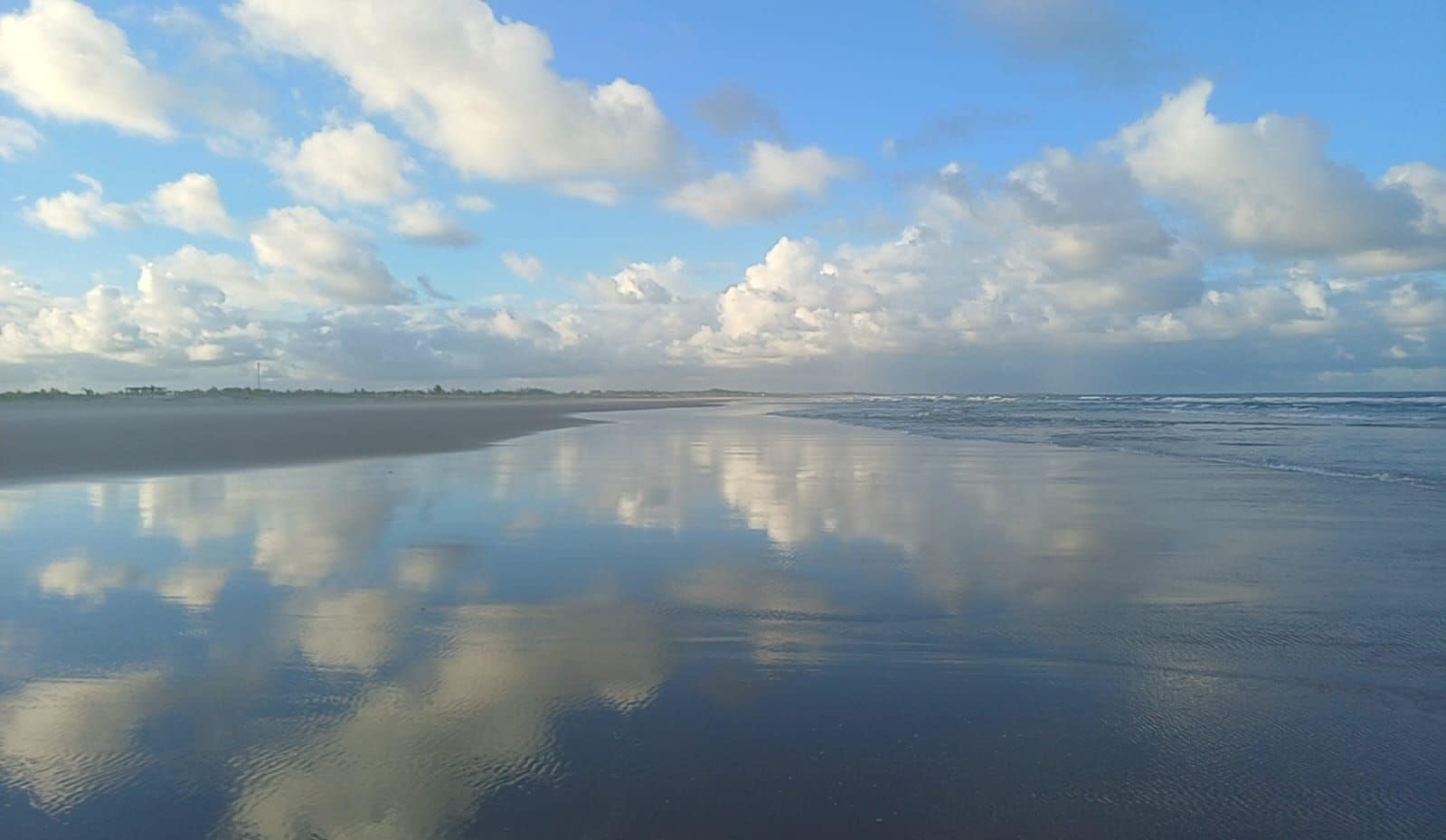 A beach with a calm water surface reflecting the sky and clouds.