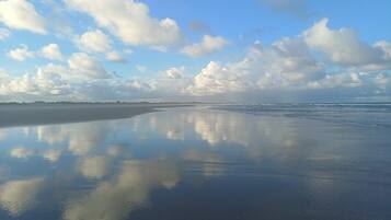 A beach with a calm water surface reflecting the sky and clouds.
