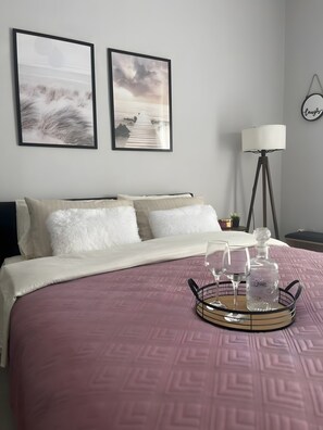 A neatly made bed with a pink bedspread, two framed pictures on the wall, a floor lamp, and a tray with glasses and a bottle on the bed. - Apartment 'George House' with Balcony, Wi-Fi and Air Conditioning (Θεσσαλονίκη)
