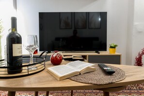 A room with a television, a wine bottle, a glass, a book, and a remote control on a wooden table. - Apartment 'George House' with Balcony, Wi-Fi and Air Conditioning (Θεσσαλονίκη)