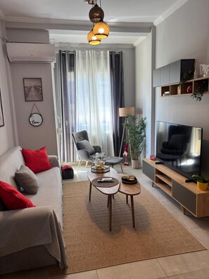 A modern living room with a sofa, coffee table, TV stand, and a large window with curtains. - Apartment 'George House' with Balcony, Wi-Fi and Air Conditioning (Θεσσαλονίκη)