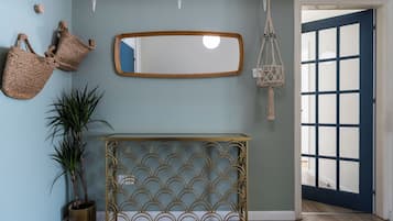 Un corridoio con una porta blu, un tavolo consolle dorato e decorazioni a parete, tra cui uno specchio e arazzi in macramè.