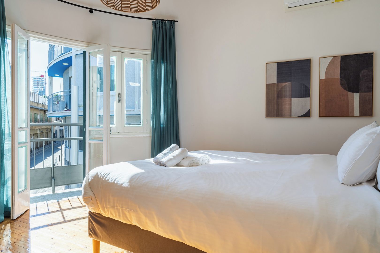Una camera d'albergo con un letto, un balcone e due quadri astratti appesi al muro.