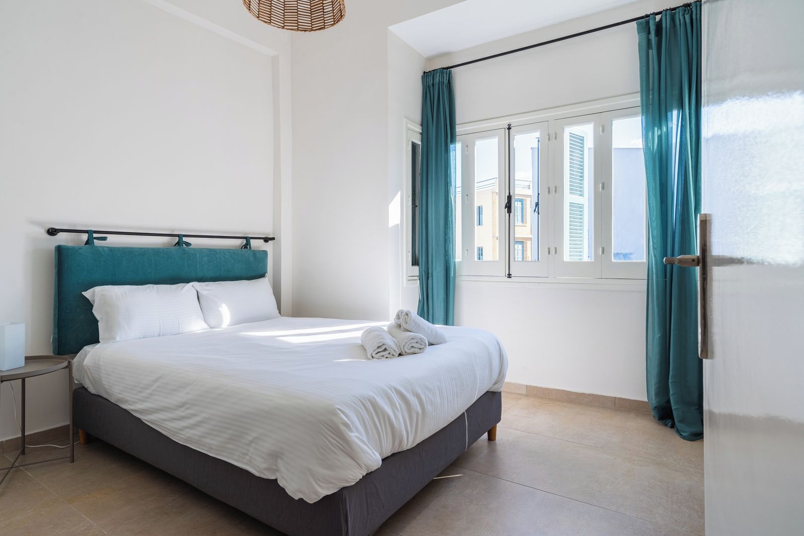 Une chambre d’hôtel avec un lit, une table de chevet, une fenêtre avec des rideaux et une porte.