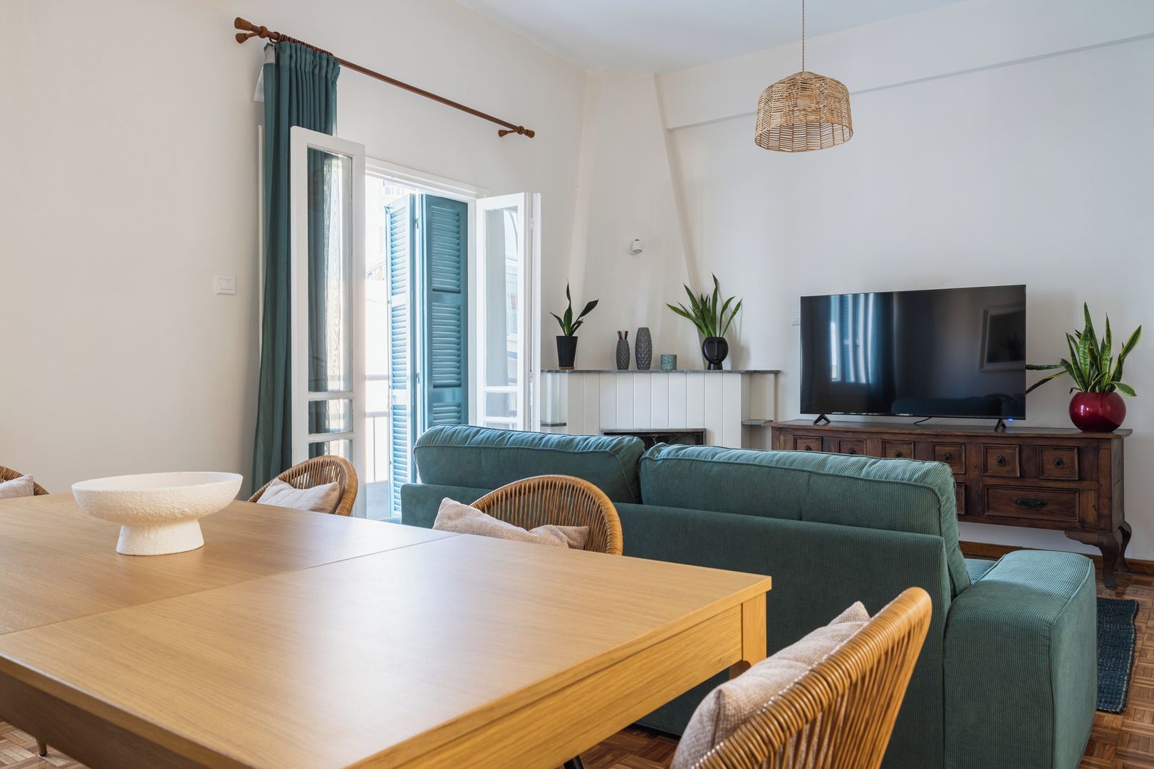 Un soggiorno con un tavolo da pranzo in legno, un divano verde e una televisione su un mobiletto in legno.