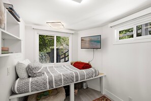 A modern bedroom with a built-in bed, a TV mounted on the wall, and a window with a view of greenery. - Private Ocean-View Guest Casita, South Laguna Beach (Laguna Beach)