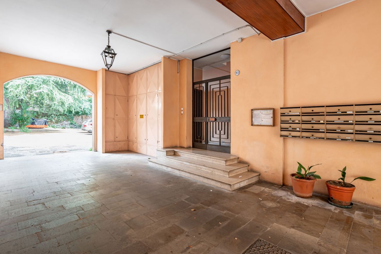 A hotel entrance with a tiled floor, a wooden door, a metal gate, and a wall-mounted mailbox.