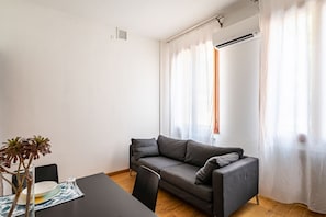 A modern living room with a grey sofa, a dining table with chairs, and a small plant. - GuestHost - Padova Suite Isabella 500m from the Duomo! (Padova)