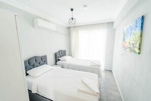 Ein modernes Hotelzimmer mit zwei Betten, einem großen Fenster mit transparenten Vorhängen, einem Bild an der Wand und einer Klimaanlage.