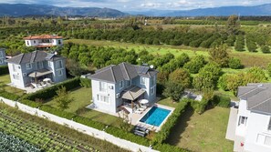 Una casa moderna de dos pisos con piscina, rodeada de exuberante vegetación y vistas a montañas distantes.