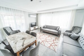 Ein modernes Wohnzimmer mit einem Marmortisch, grauen Polstersofas und einem Fernseher auf einem weißen Schrank.