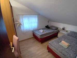 A bedroom with two beds, a window with sheer curtains, a bedside table with a lamp, and a door with a number. - Serene 6-bedroom house in Vrelo Koreničko perfect for groups (Vrelo Koreničko)