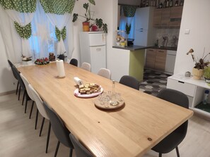 A dining area with a wooden table, chairs, a kitchen in the background, and a potted plant on the counter. - Serene 6-bedroom house in Vrelo Koreničko perfect for groups (Vrelo Koreničko)