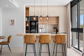 Eine moderne Küche mit Bar, Pendelleuchten und Blick durch große Fenster.
