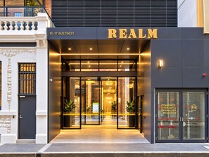 A hotel entrance with a modern design, featuring a glass door entrance, a sign with the name 'REALM', and a visible fire hydrant on the right. - Koala Stay Luxury CBD Retreat with Skyline Views (Adelaide)