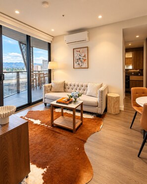 A modern living room with a sofa, coffee table, and a view through large windows. - Koala Stay Luxury CBD Retreat with Skyline Views (Adelaide)