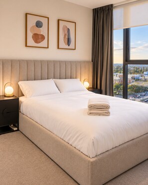 A hotel room with a large bed, two bedside tables, a view of the city, and abstract art on the wall. - Koala Stay Luxury CBD Retreat with Skyline Views (Adelaide)