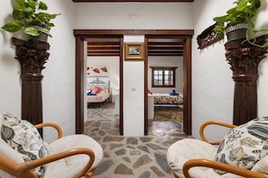 Quarto com soalho de pedra, duas camas com roupa de cama florida, uma cadeira de madeira e uma planta em vaso.