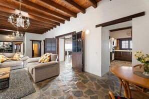 Ampla sala de estar com piso de pedra, teto de madeira e mesa de jantar com cadeiras.