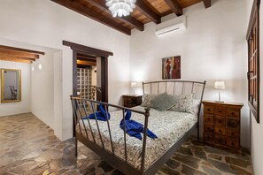 A bedroom with a stone floor, a bed with patterned bedding, a wooden headboard, a nightstand with a lamp, and a dresser with drawers. - Villa Finca Vicela - Five Bedroom Villa, Sleeps 10 (Tias)