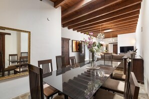 Uma sala de jantar com uma mesa grande, cadeiras, um vaso com flores e teto de madeira.