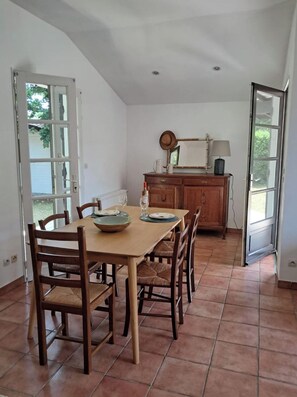 A dining area with a wooden table and chairs, a cabinet with a lamp, and a view through a glass door. - Family home 500 meters from the beach, sleeps 6 (Andernos-les-Bains)