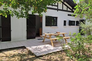 A white building with black shutters, a wooden table with benches, and a tiled patio area. - Family home 500 meters from the beach, sleeps 6 (Andernos-les-Bains)