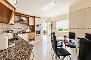 A modern kitchen with granite countertops, stainless steel appliances, and a dining area with a glass table and black chairs. - Villa Girassol - Three Bedroom Villa, Sleeps 6 (Vale Rebelho)