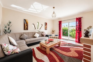 A modern living room with a sofa, coffee table, and a view of the outdoors through a sliding glass door. - Villa Girassol - Three Bedroom Villa, Sleeps 6 (Vale Rebelho)