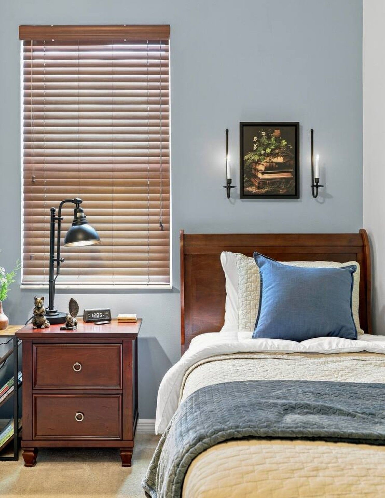 Una camera da letto con un letto, un comodino con una lampada, una sveglia a parete e un quadro incorniciato.