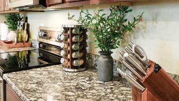 A kitchen with granite countertops, a stainless steel range hood, a unique spice rack, a potted plant, and a knife block.