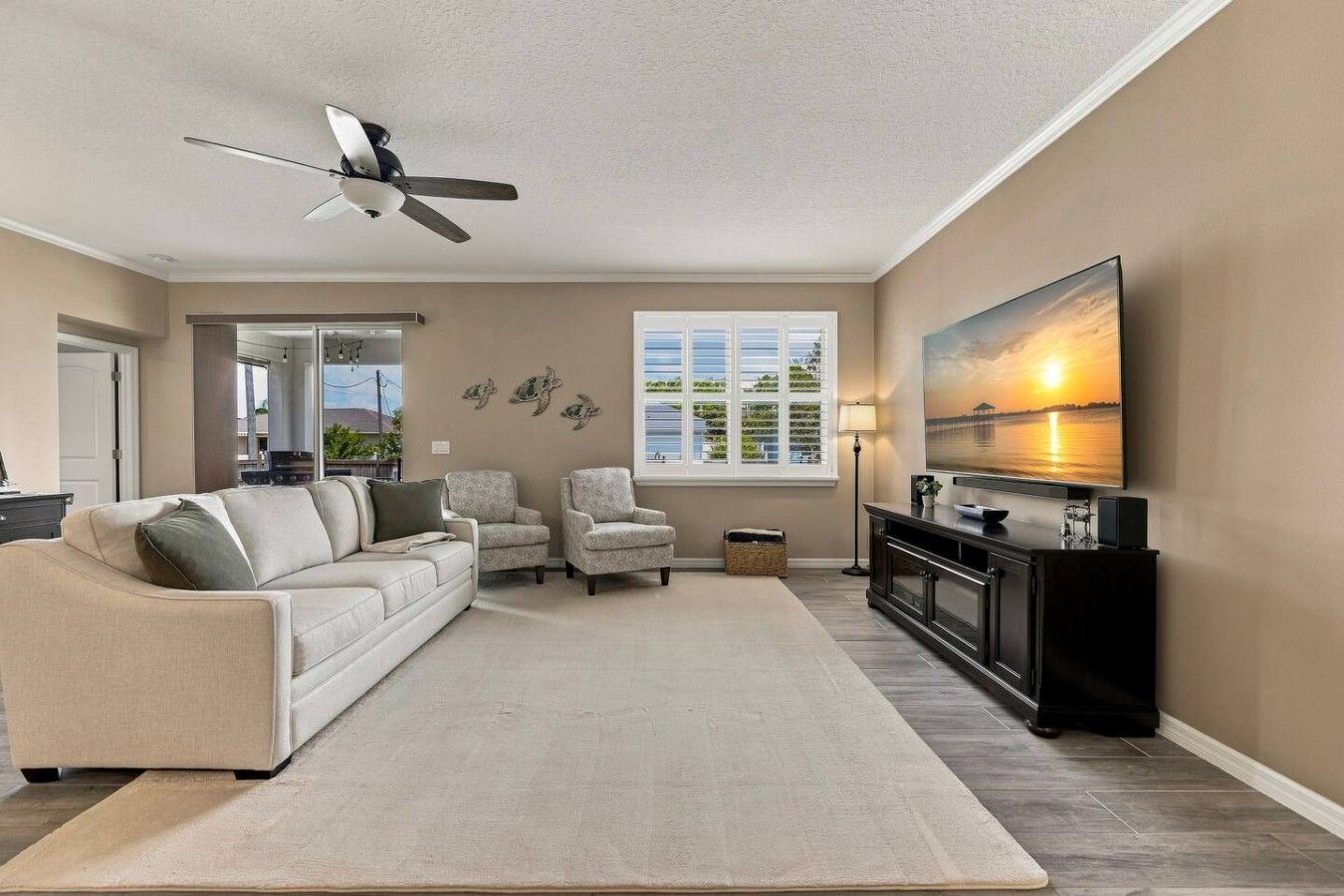 Un salon comprenant un canapé, deux fauteuils, un téléviseur et un ventilateur de plafond.