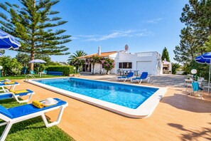 Ein Swimmingpool mit Liegestühlen und Sonnenschirmen, umgeben von Grünflächen und einem Gebäude mit einem Ziegeldach.