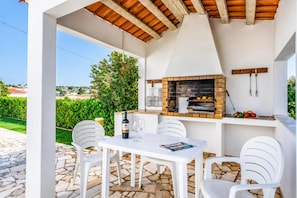 Eine Terrasse im Freien mit Steinboden, weißer Möbel, einem Backofen aus Ziegeln und Blick auf die Landschaft.