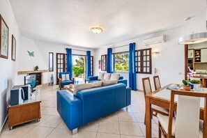 Een ruime woonkamer met een blauwe bank, een eettafel met stoelen en een open haard.