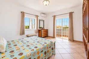 Ein Schlafzimmer mit einem Bett, einem Schminktisch, einer Bank und einer Glastür, die auf einen Balkon führt.