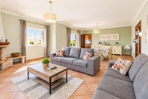 A living room with a grey sofa, a wooden coffee table, and a dining area with a white table and chairs. - Villa Silva Balbina - Four Bedroom Villa, Sleeps 8 (Albufeira)