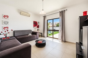 A modern living room with a sofa, a coffee table, and a TV stand. There is a window with curtains, a lamp, and artwork on the walls. - Villa Dela - Two Bedroom Villa, Sleeps 4 (Vale Rebelho)
