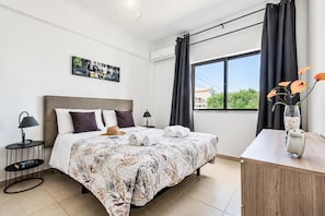 A hotel room with a bed, a bedside table, a lamp, a painting on the wall, a window with curtains, and a vase with flowers. - Villa Dela - Two Bedroom Villa, Sleeps 4 (Vale Rebelho)